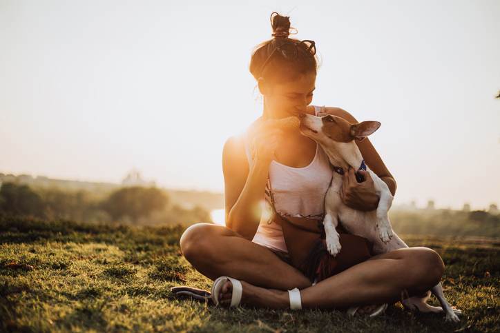 Young, beautiful and smiling girl enjoying with a dog in a public park in the city. She plays with him, eating ice cream, race and throwing his stick. Their time is filled with love and happiness.