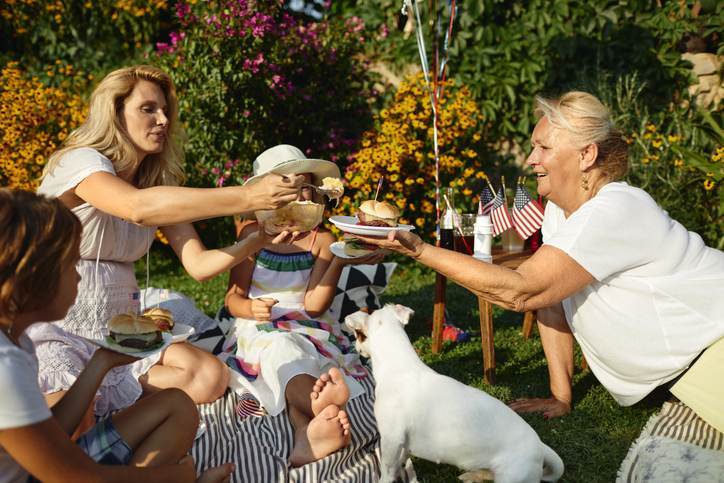 Multi-generation family on picnic in back yard sitting on blanket, eating burgers and celebrating 4th of July - Independence Day.