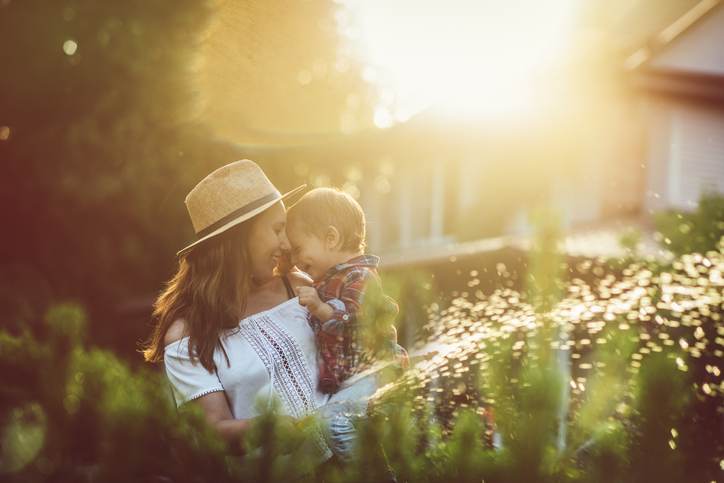 Mother and her little sun watering plants in garden in summer